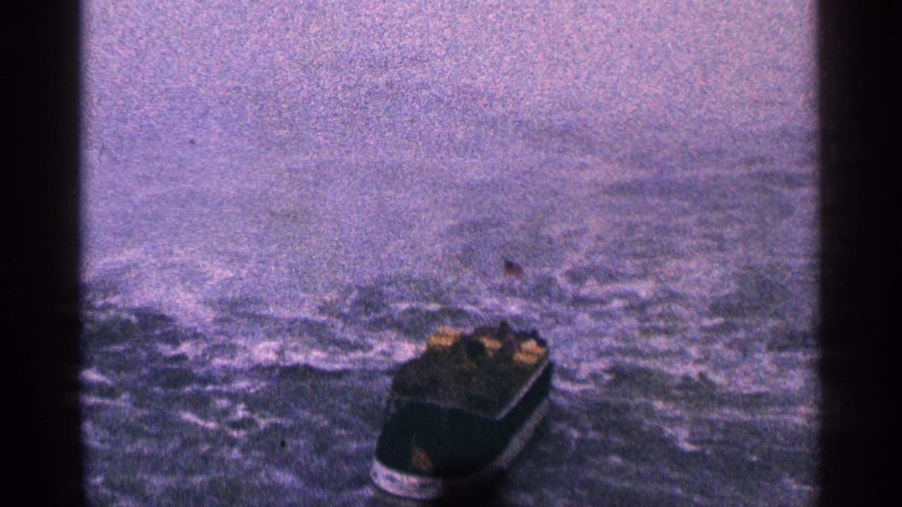 Small dark boat moving across choppy grey-blue water under an overcast sky.