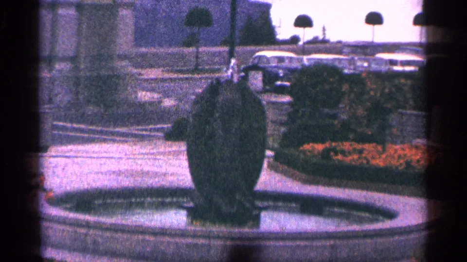 1964 Niagara Falls, Canada travel frame showing a bubbling garden fountain with flowers, shrubs, and mid-century parked cars behind it.
