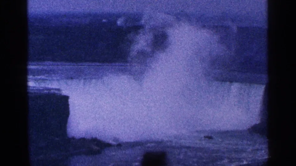 Blue-tinted 1964 Niagara Falls home-movie frame showing dense mist above the river with soft focus and visible 8mm frame edges.