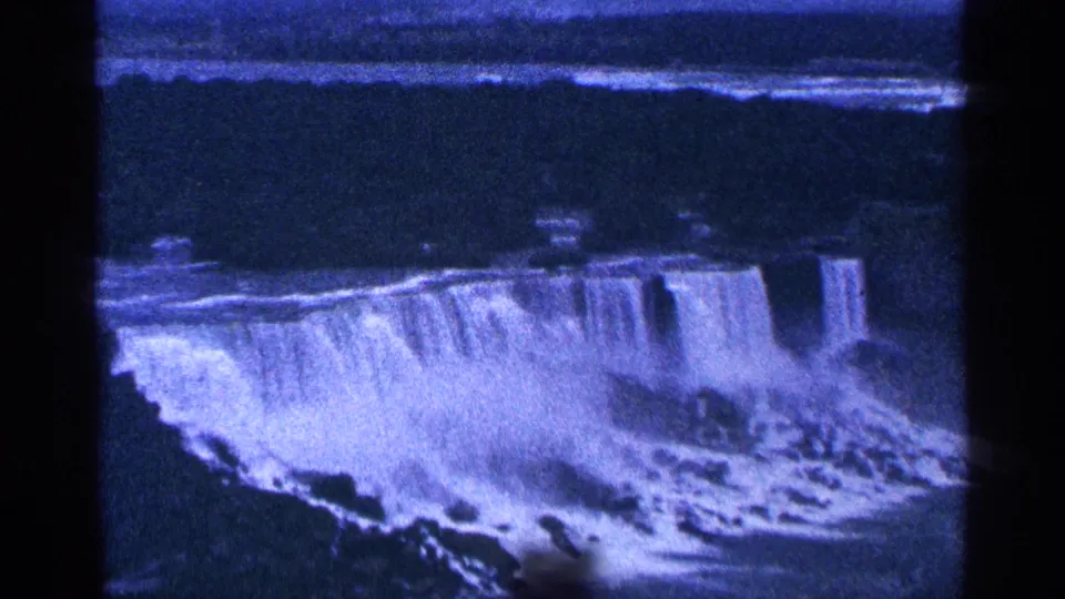 1964 8mm home-movie frame showing Niagara Falls in Canada, with the waterfall spanning the lower frame and mist drifting across the gorge.