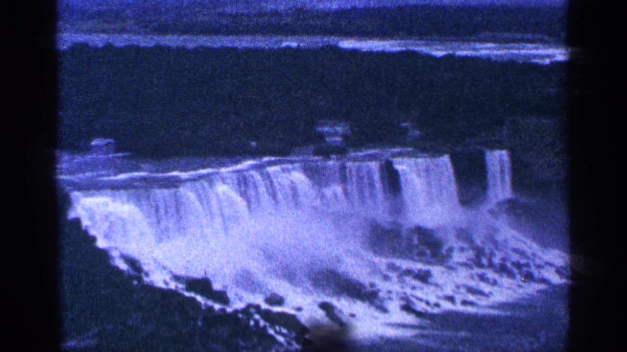 Blue-tinted view of Niagara Falls with water cascading over the edge and mist below.