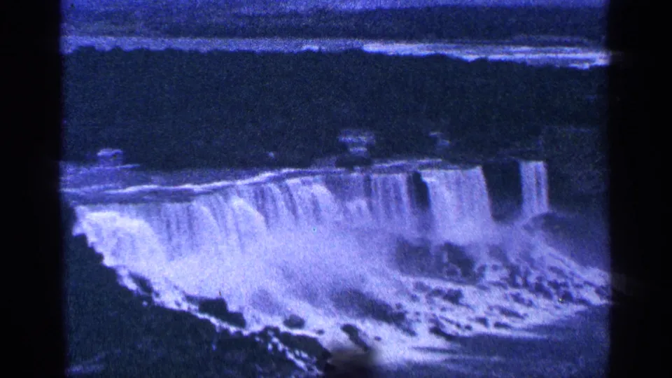 1964 8mm home-movie view of Niagara Falls in Canada, showing broad cascades, river water, mist, and dark film borders.