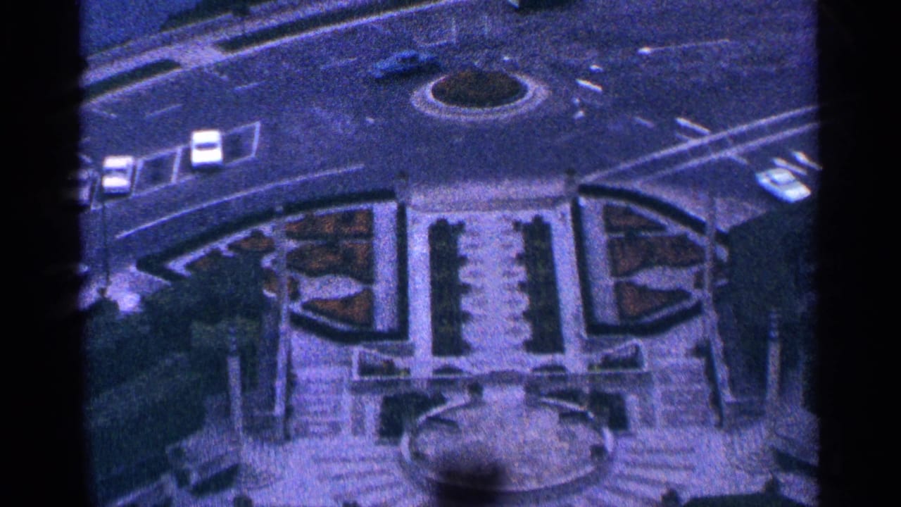 High-angle view of a circular traffic island, streets, cars, gardens, and steps.
