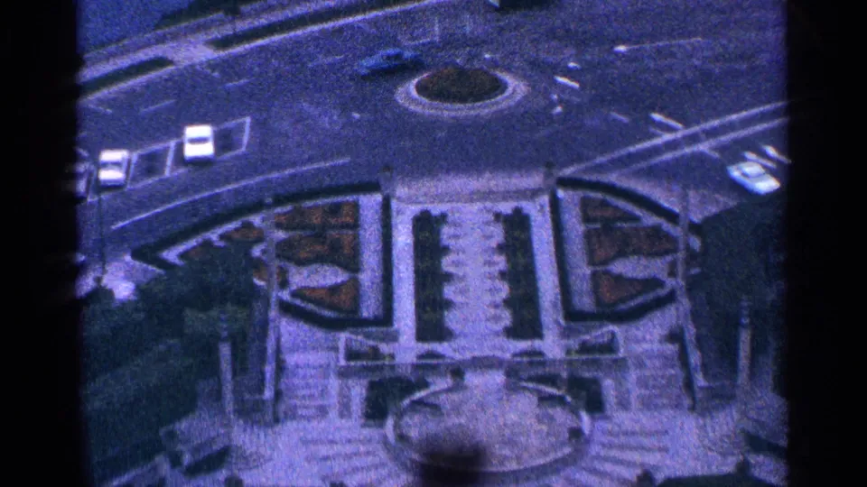 High-angle 1964 view in Niagara Falls, Canada, showing a round traffic island, cars, formal garden beds, stairs, and a fountain area.