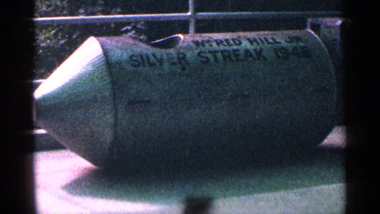 1964 Niagara Falls home-movie frame showing a green stunt barrel marked Silver Streak in an outdoor display area.