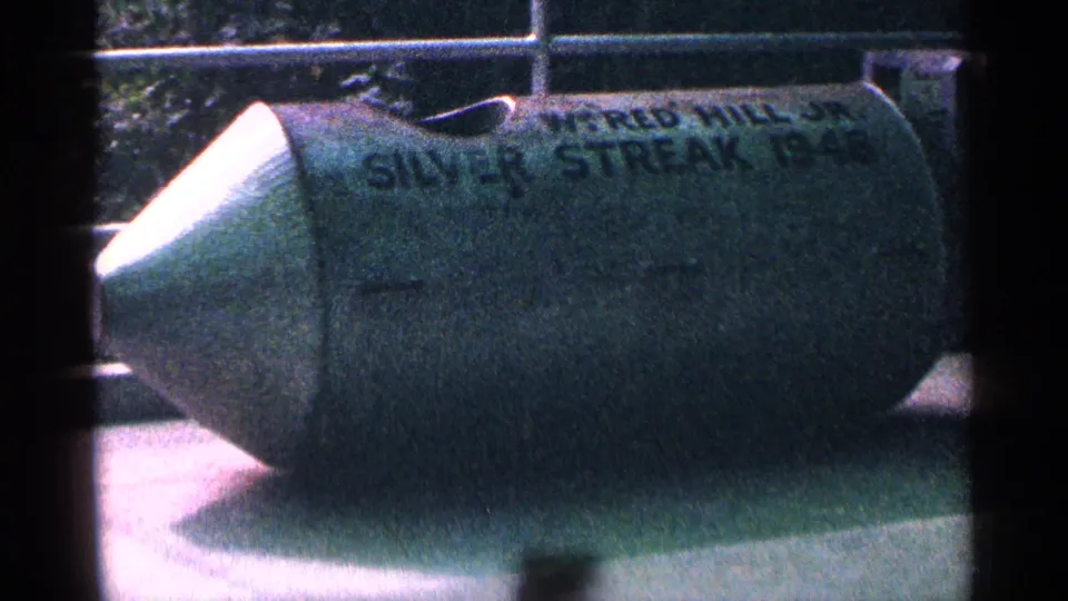 1964 Niagara Falls home-movie frame showing a green stunt barrel marked Silver Streak in an outdoor display area.