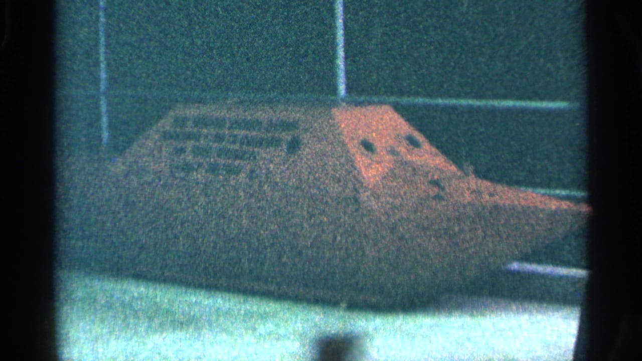 Dark steamship model with rust-colored panels in front of a blue-green wall display.