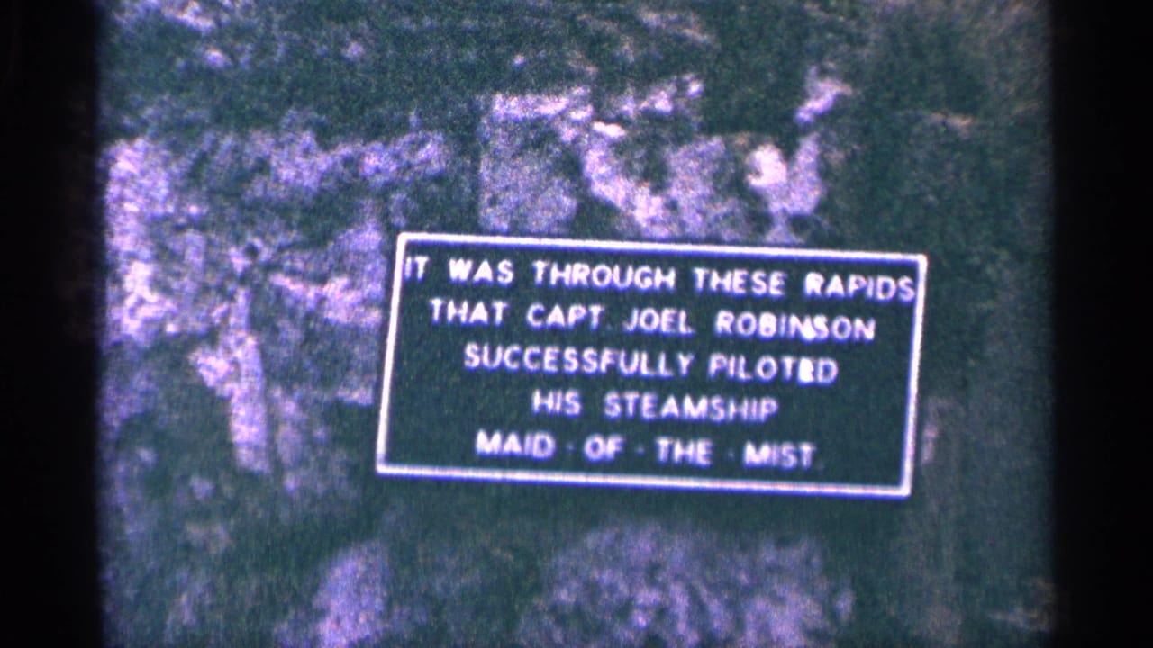 1964 8mm frame showing a sign on rock about Captain Joel Robinson piloting Maid of the Mist through rapids.
