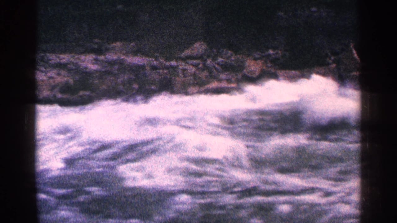 Churning rapids flow past dark rocks with white water filling the lower frame.