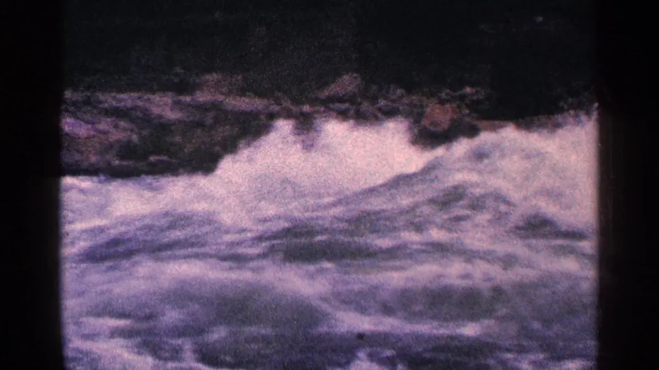 Grainy 1964 8mm view of Niagara Falls Canada rapids, with foaming water below a rocky edge.