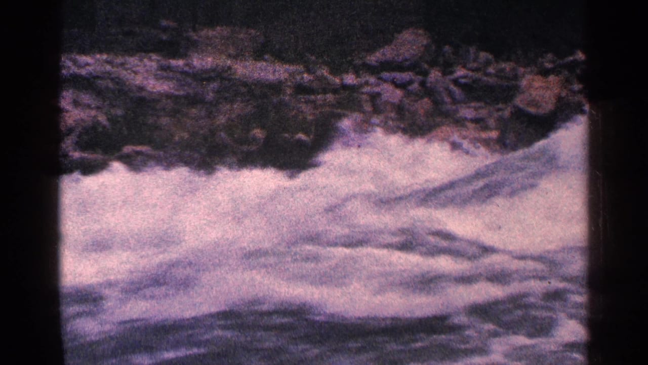 Foaming river water rushing past dark rocks in a faded 8mm frame.