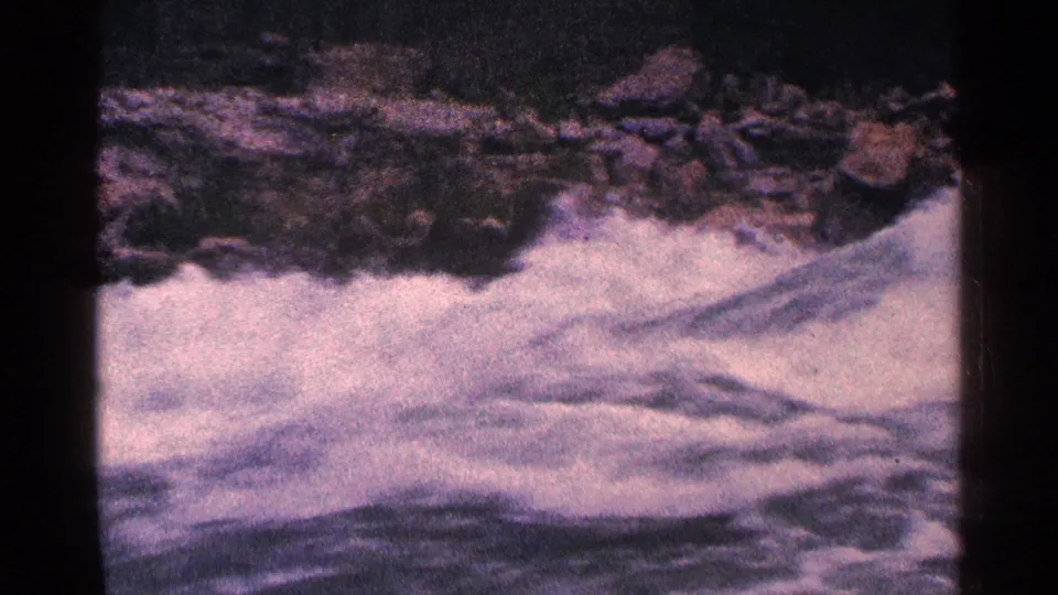 1964 8mm home-movie frame of rushing water and dark rocks at Niagara Falls, Canada, with faded magenta-blue color shift.