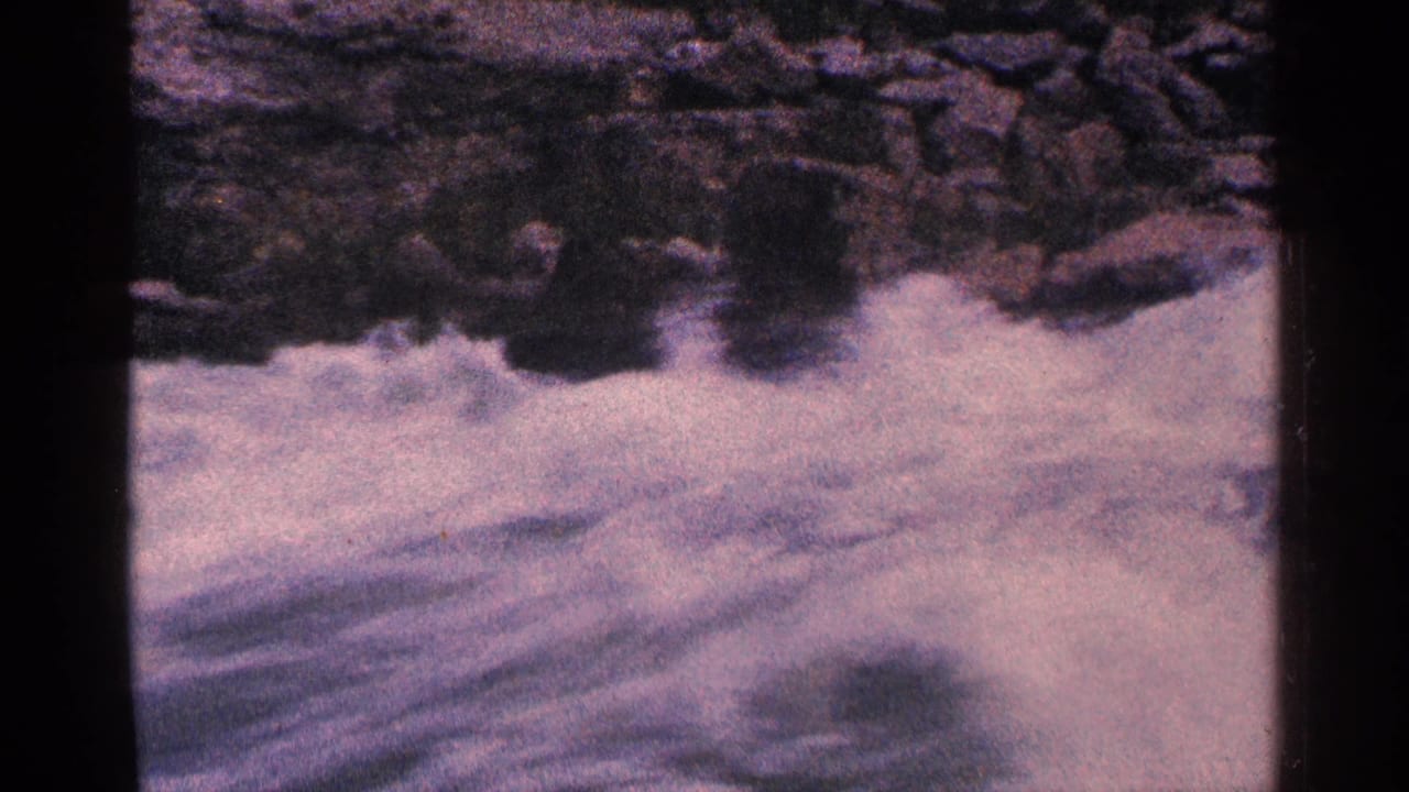 Fast whitewater breaks around rocks with soft focus and aged color.
