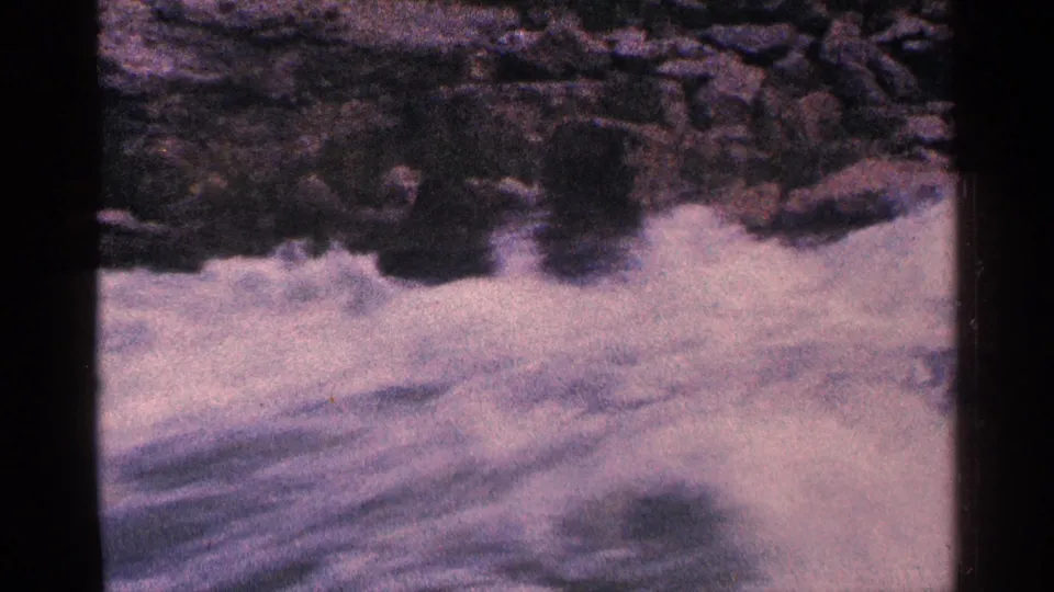 Rushing river water near Niagara Falls, Canada, fills the 1964 8mm frame, with rocks along the upper edge and visible film grain.