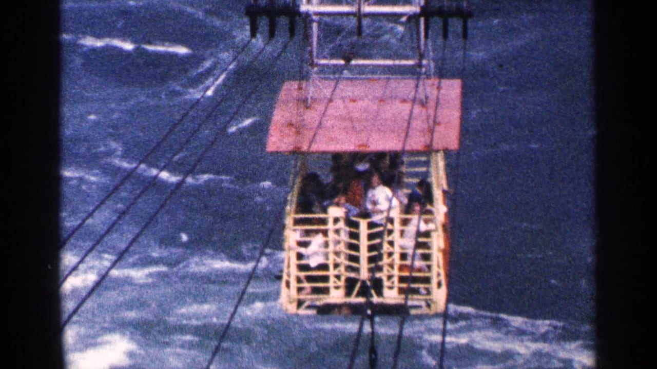 Open cable car carrying passengers above turbulent blue water.