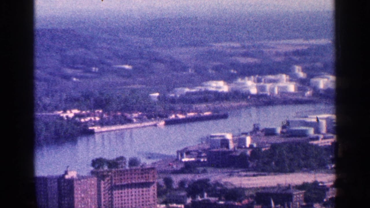 Elevated view across a wide river toward industrial buildings and storage tanks.