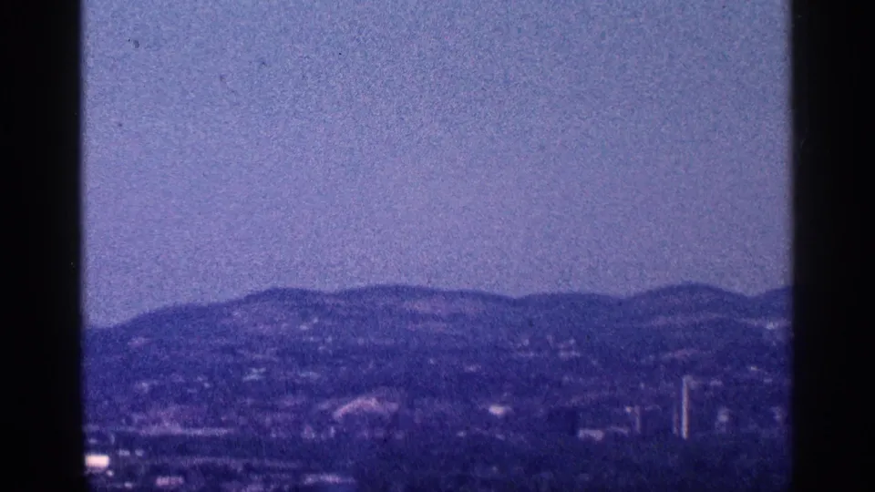Soft 8mm frame of distant wooded hills, scattered buildings, and a vertical structure in the likely Niagara Falls, Canada area.