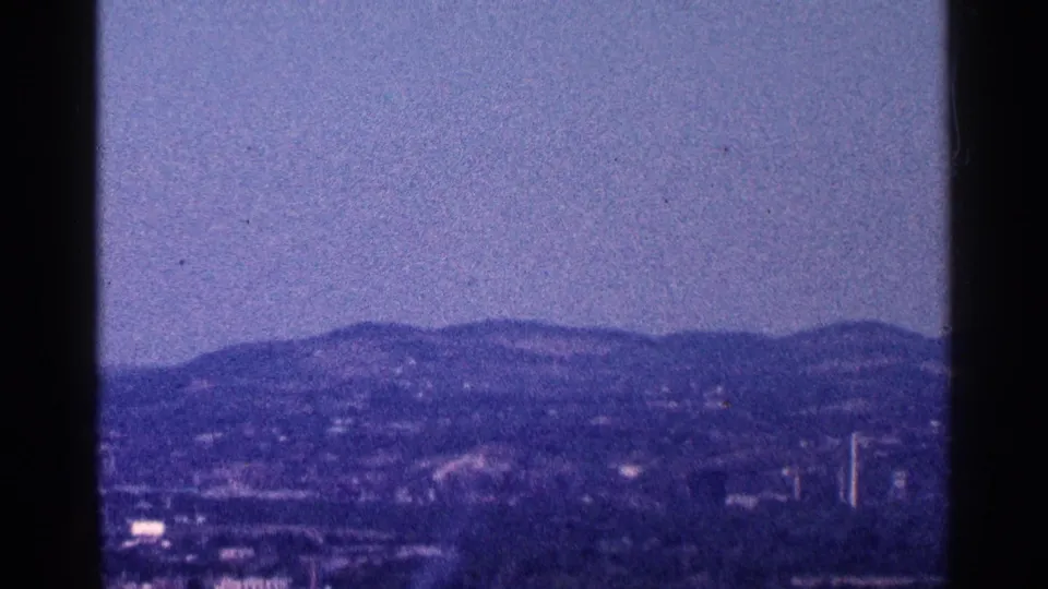 End frame from the 1964 home movie showing distant hills, scattered development, and dark foreground foliage near the Niagara Falls area.