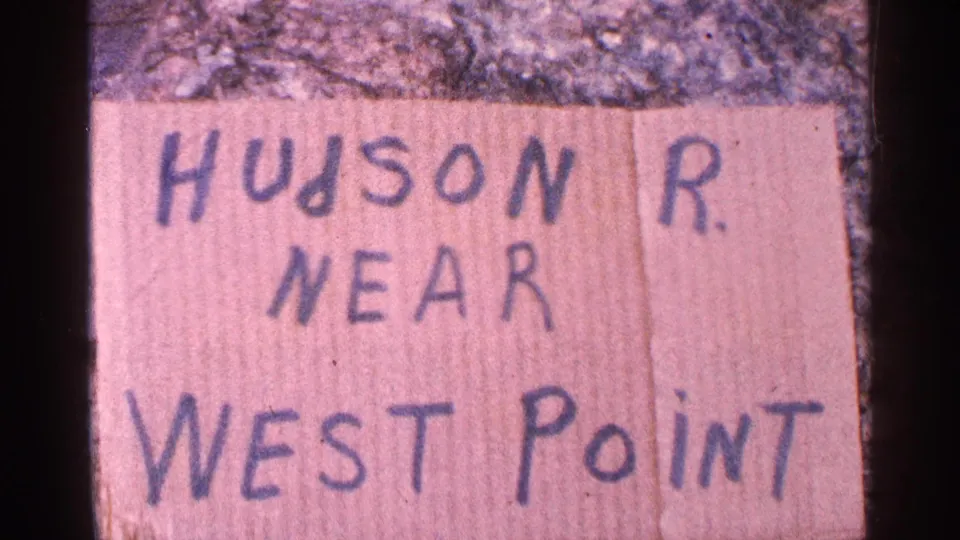 Closer 8mm frame of the handwritten HUDSON R. NEAR WEST POINT card, with rough ground visible above it.