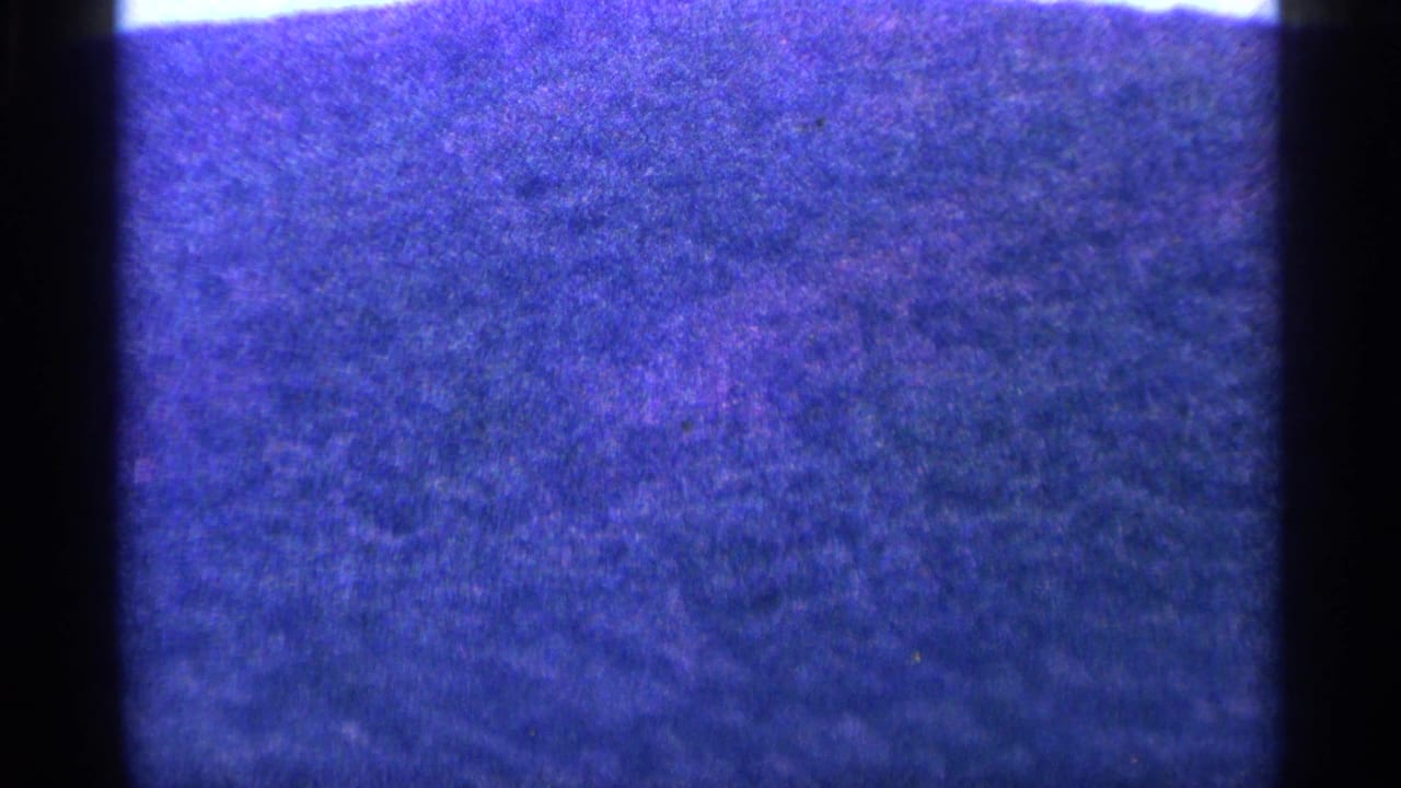 Blue-tinted grainy frame with dark film gate edges and no clear subject detail.