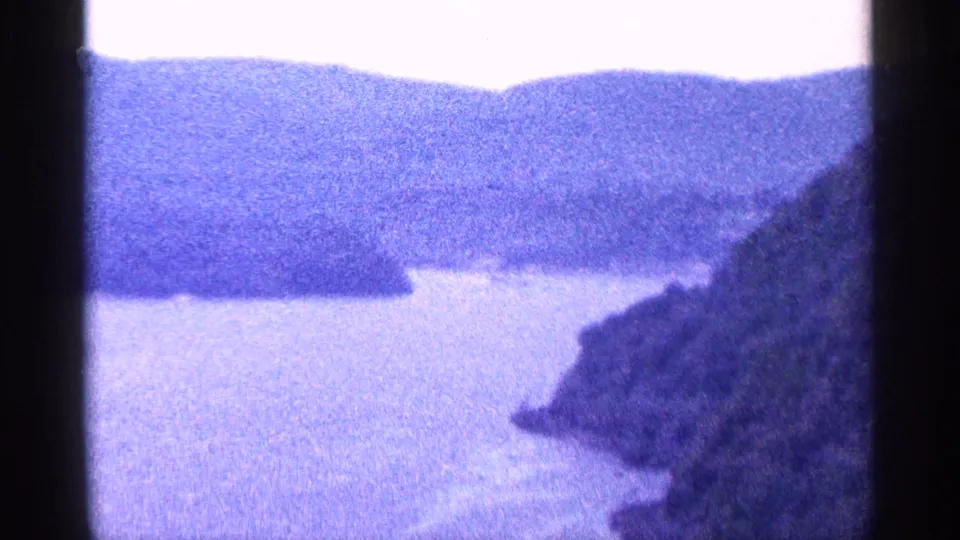 1964 Niagara-area home-movie view of a broad river or inlet, distant hills, bright sky, and rocky shoreline.