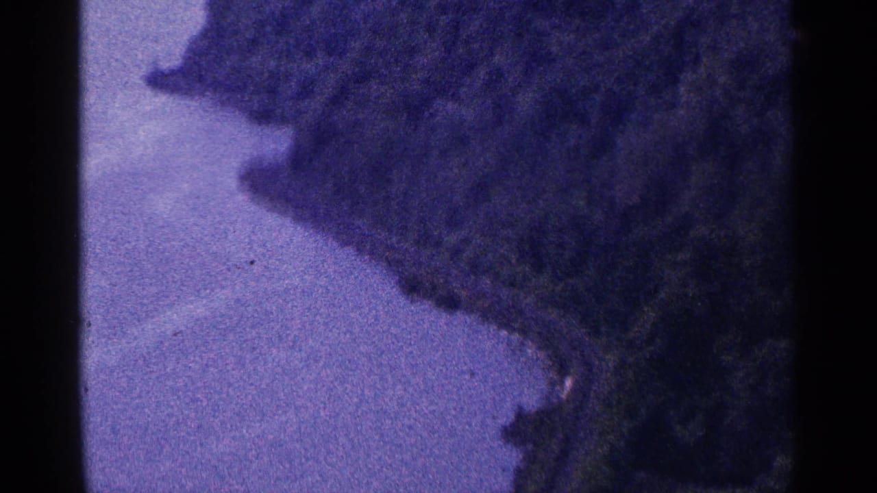 Narrow waterway bordered by a dark forested slope and distant shoreline.