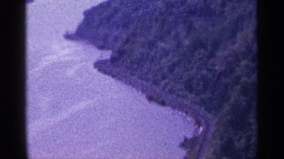 Final 1964 8mm frame holding on calm water and a wooded bank, with visible grain, soft exposure, and a purple film shift.
