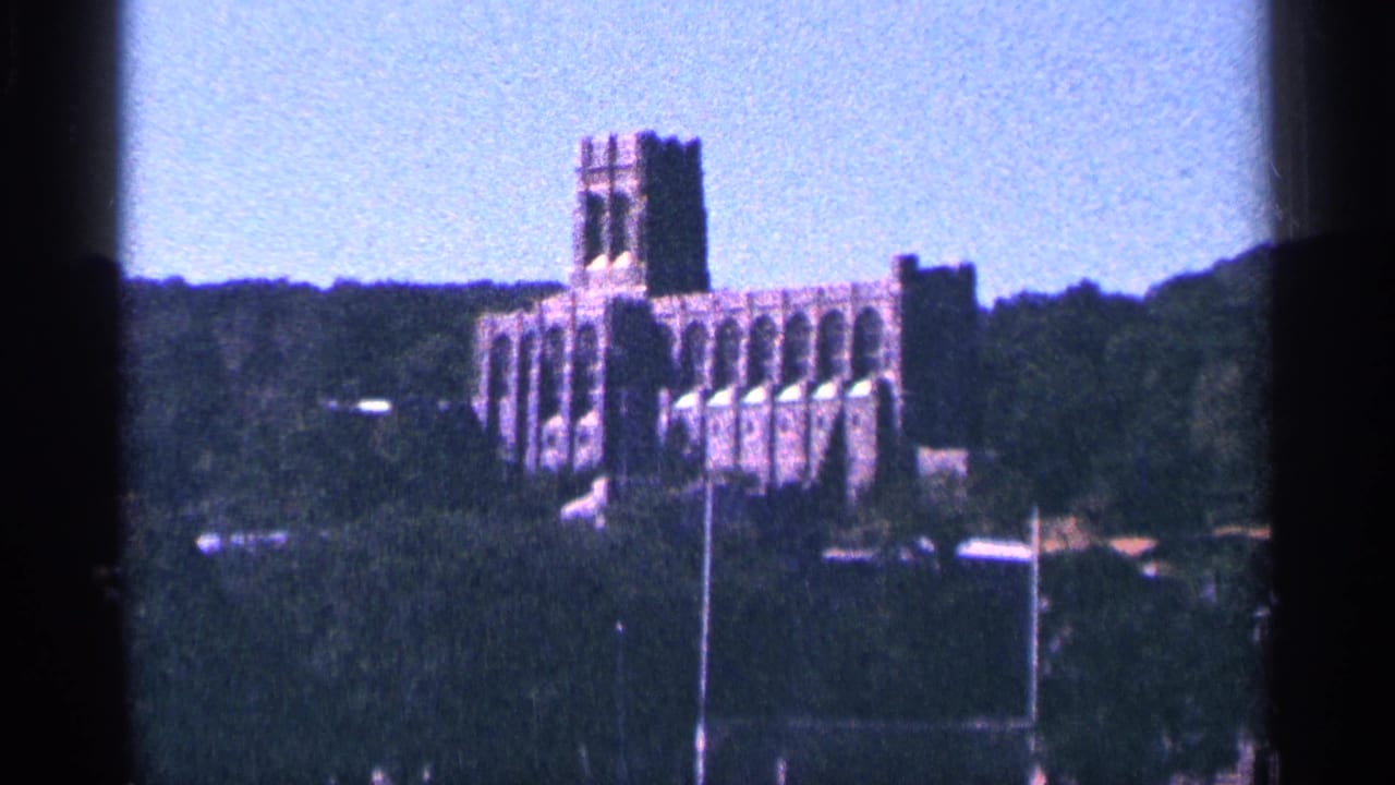 Large towered building seen across trees with field posts in the foreground.