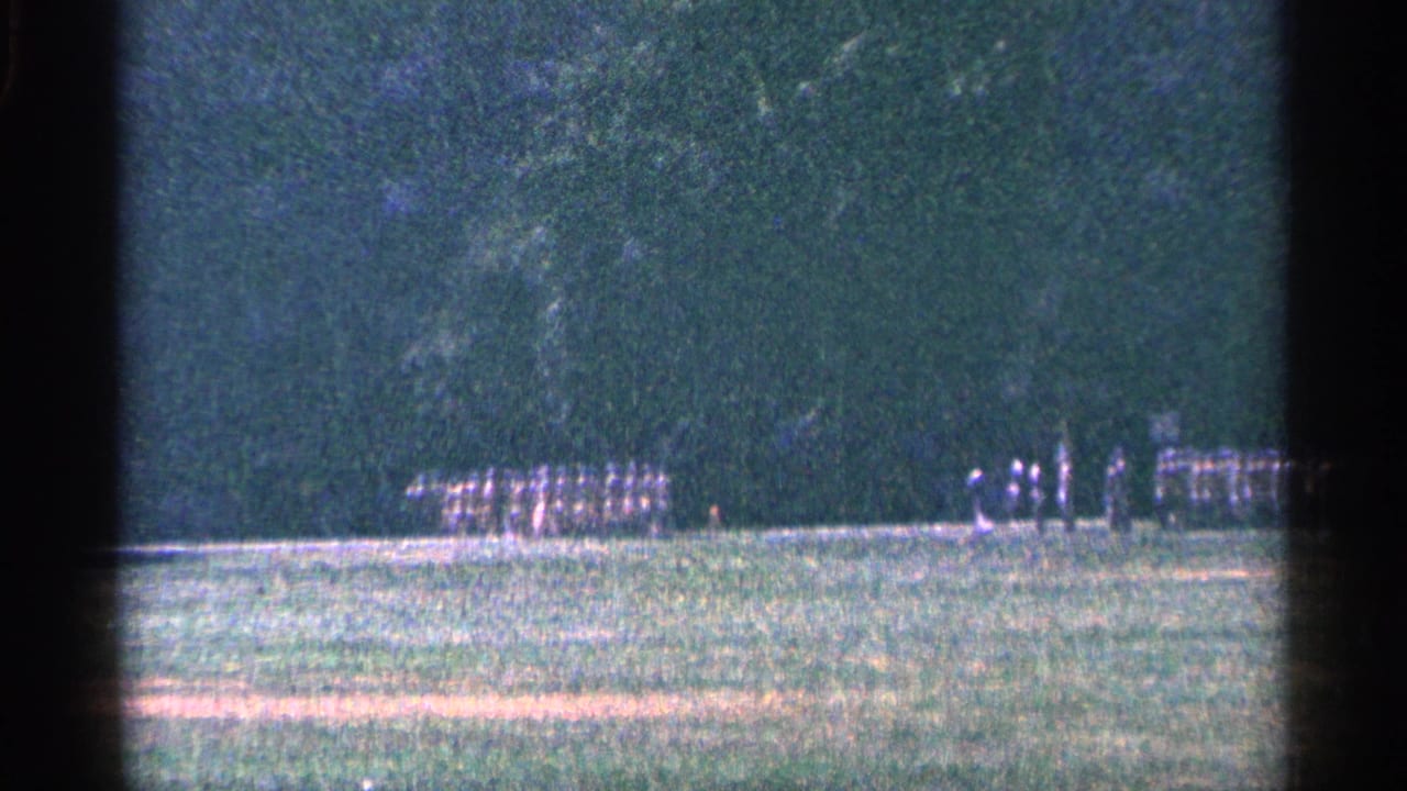 1964 Niagara Falls, Canada 8mm frame showing distant uniformed men in formation on grass with trees behind them.