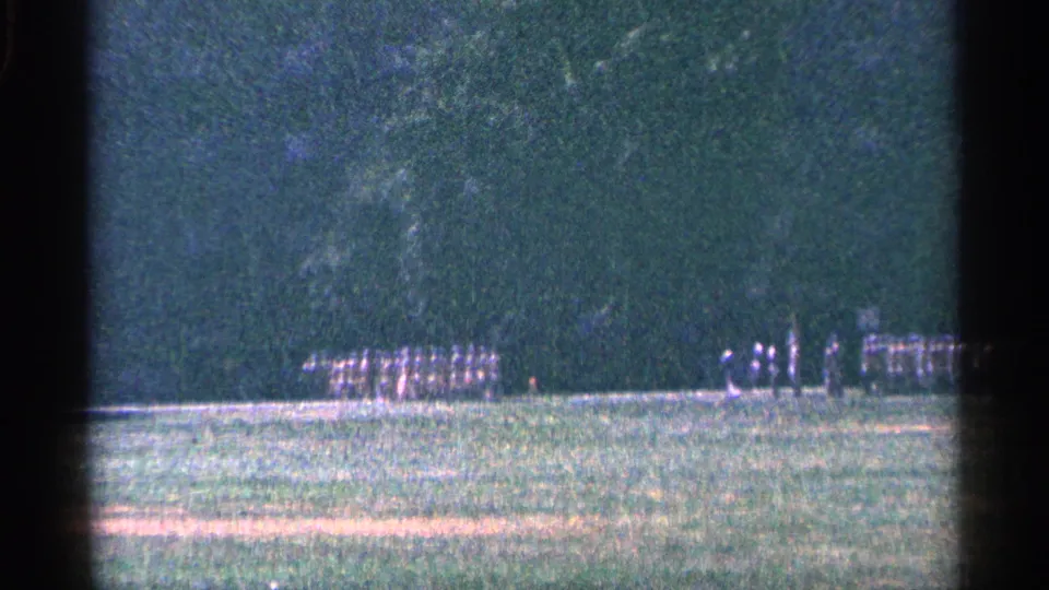 1964 Niagara Falls, Canada 8mm frame showing distant uniformed men in formation on grass with trees behind them.