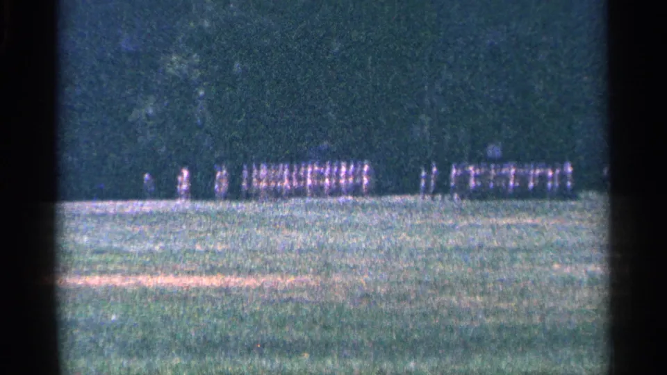 Distant 1964 Niagara Falls, Canada frame showing uniformed men in a larger formation with other figures nearby.