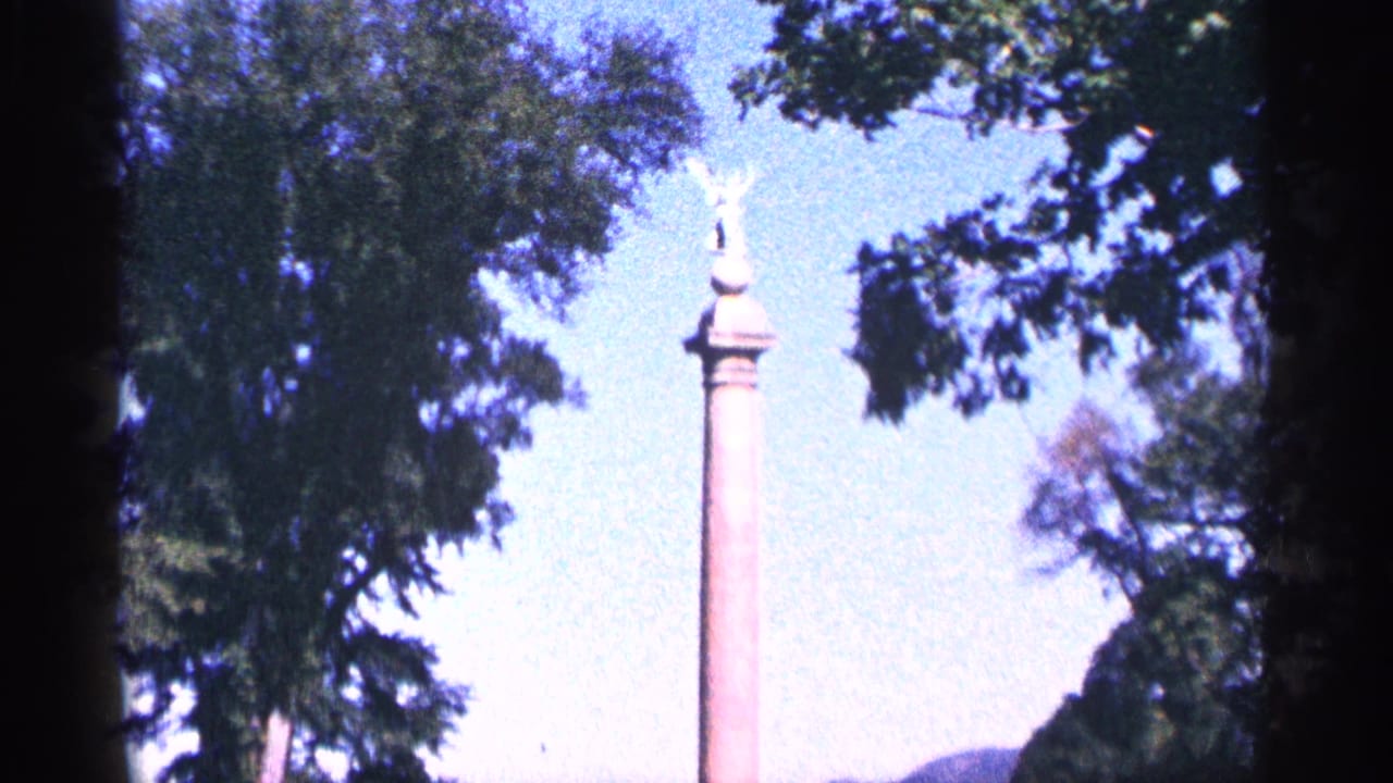 Tall column with a winged statue at the top, framed by trees and blue sky.
