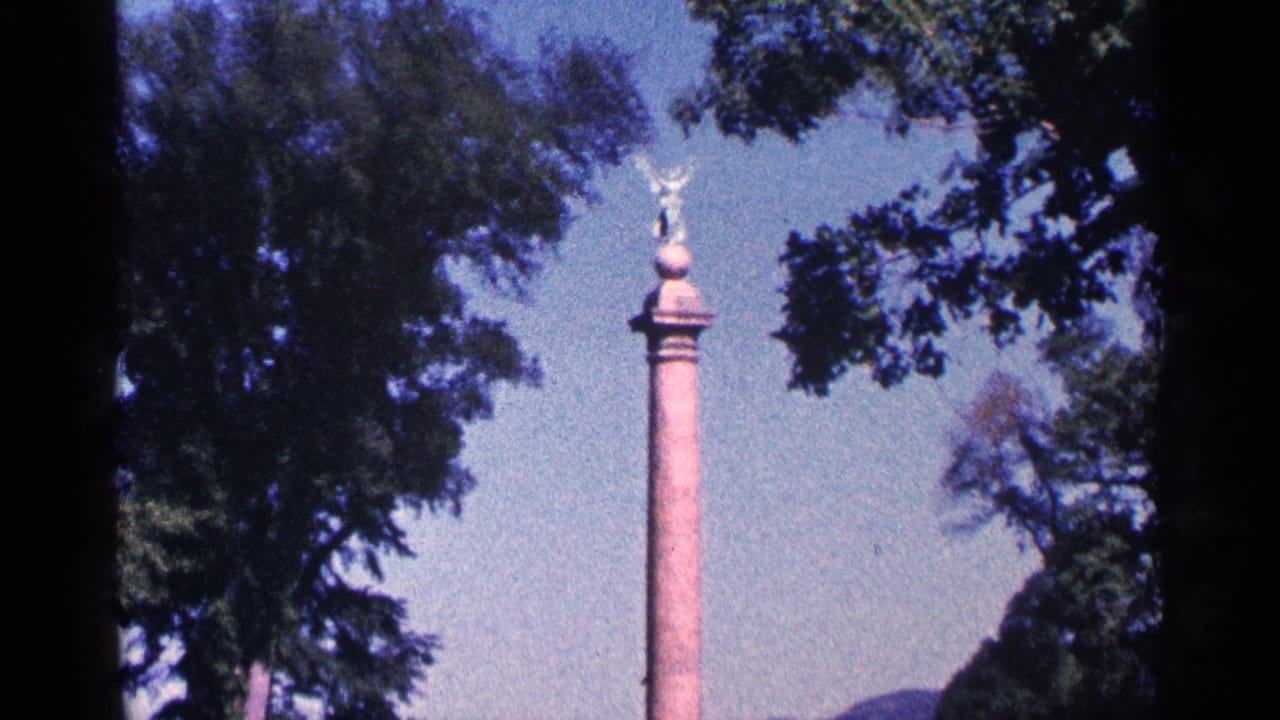 Tall commemorative column with a winged statue at the top, filmed through trees in 1964 Niagara Falls, Canada footage metadata.