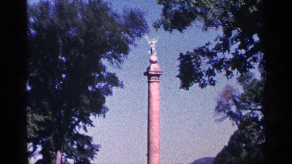 Tall commemorative column with a winged statue at the top, filmed through trees in 1964 Niagara Falls, Canada footage metadata.
