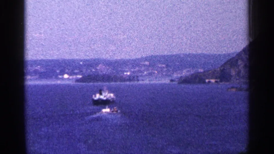 A distant boat crosses the water in 1964 Niagara Falls Canada home-movie footage, with hills and shoreline behind it.