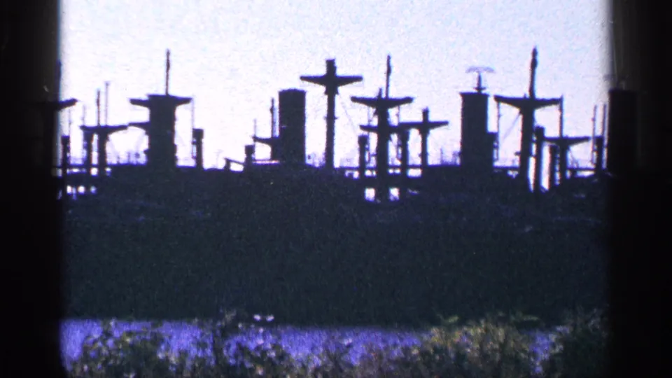 Distant 8mm view of reserve fleet ship silhouettes and vertical maritime structures along the riverbank.