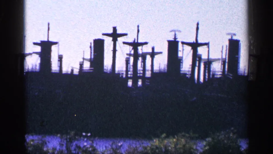 1964 8mm frame from Niagara Falls, Canada showing a distant dark ship silhouette with cross-shaped masts at dusk.