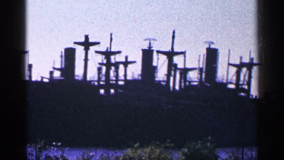 Blue-tinted 8mm frame showing a distant vessel silhouette, mast shapes, and low foreground greenery in Niagara Falls, Canada.