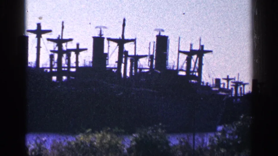 Final 8mm frame of the distant ship silhouette, with mast-like crosses, pale sky, and faint greenery in the foreground.