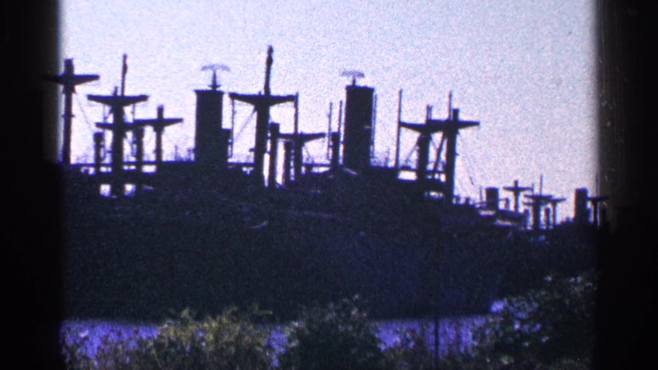 Distant ship structures silhouetted across water under a pale sky.