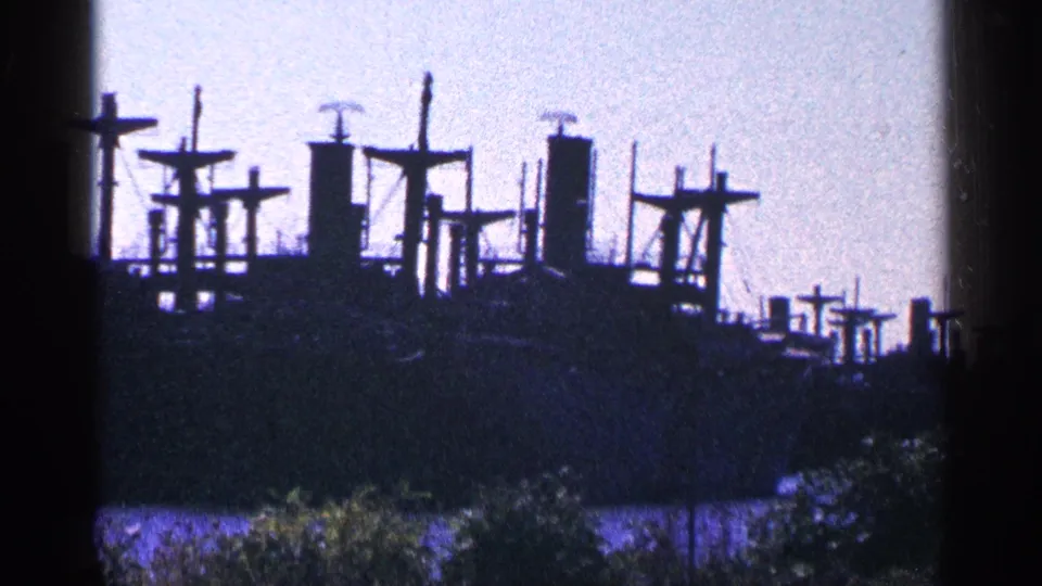 1964 8mm view near Niagara Falls, Canada, showing a distant docked ship with tall masts and cross-shaped structures across the water.