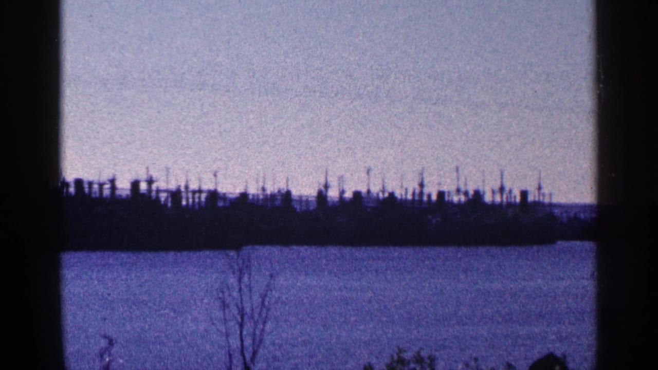 Silhouetted harbor structures stretch along the far shoreline beyond water.