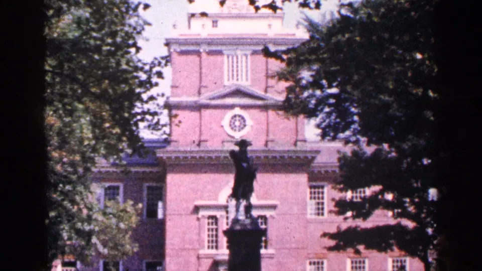 1964 Pennsylvania 8mm view of a red brick civic-looking facade with a statue on a pedestal in the foreground.