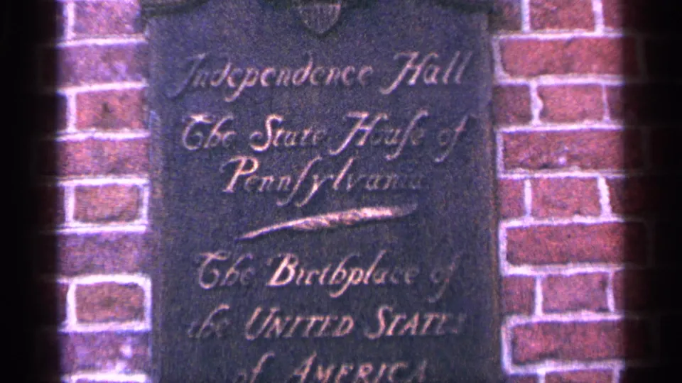 Cropped 1964 8mm view of the Independence Hall wall marker with cursive text and surrounding brickwork.