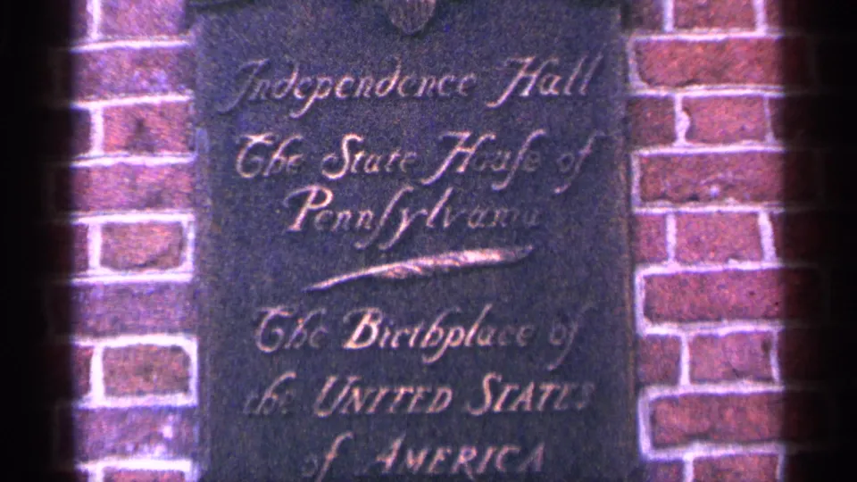 1964 Pennsylvania home-movie frame showing an Independence Hall plaque set into brickwork.