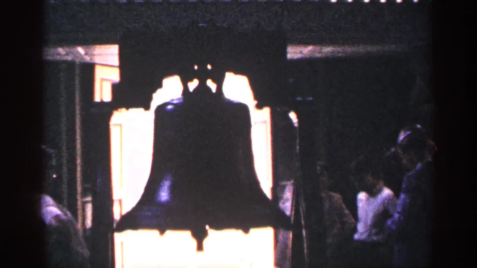 1964 Pennsylvania interior view of the Liberty Bell in silhouette against bright window light, with visitors at the sides.