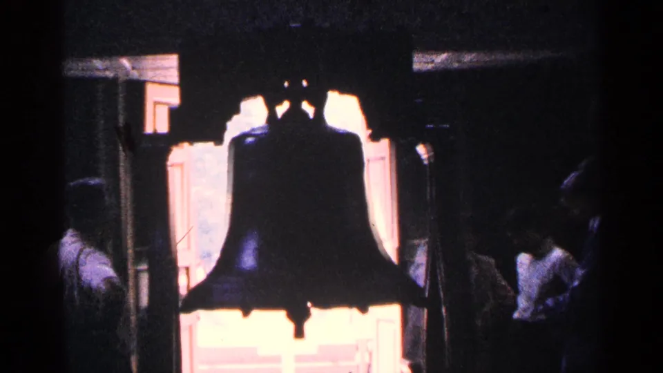 1964 Pennsylvania frame of the Liberty Bell in silhouette, framed by bright exterior light and museum visitors in shadow.