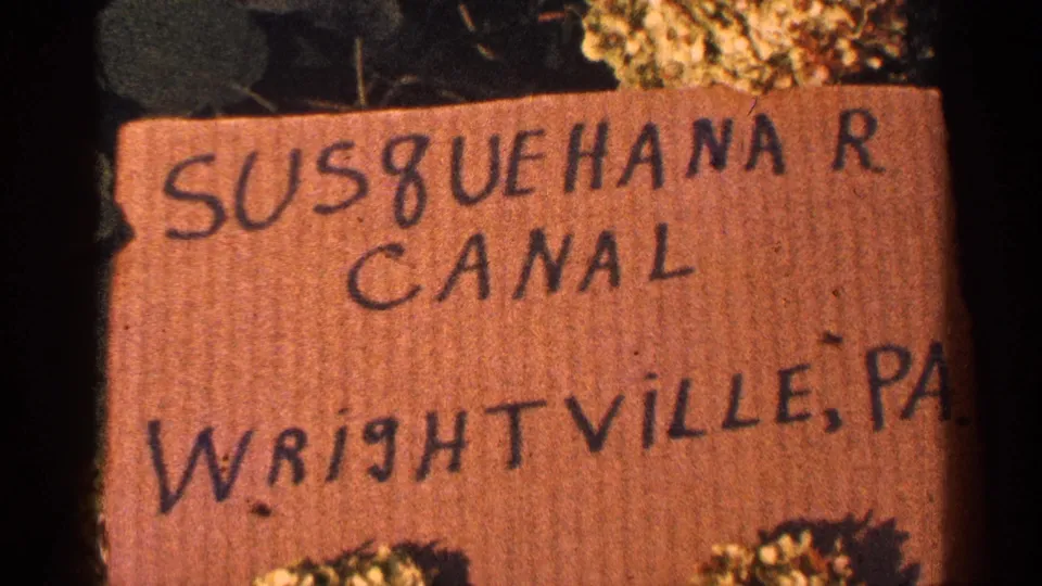 1964 Pennsylvania 8mm frame showing a hand-lettered Susquehanna River Canal sign in Wrightville with plants around the edge.