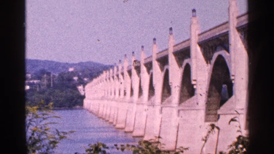1964 Pennsylvania home-movie frame showing a long arched bridge over a calm river near Gettysburg.