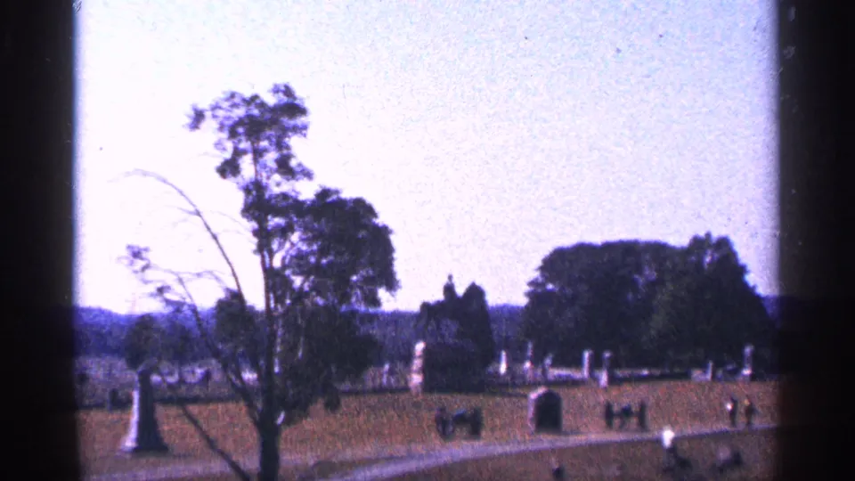 1964 Gettysburg battlefield view with monuments, open grass, trees, paths, and small figures walking in the distance.